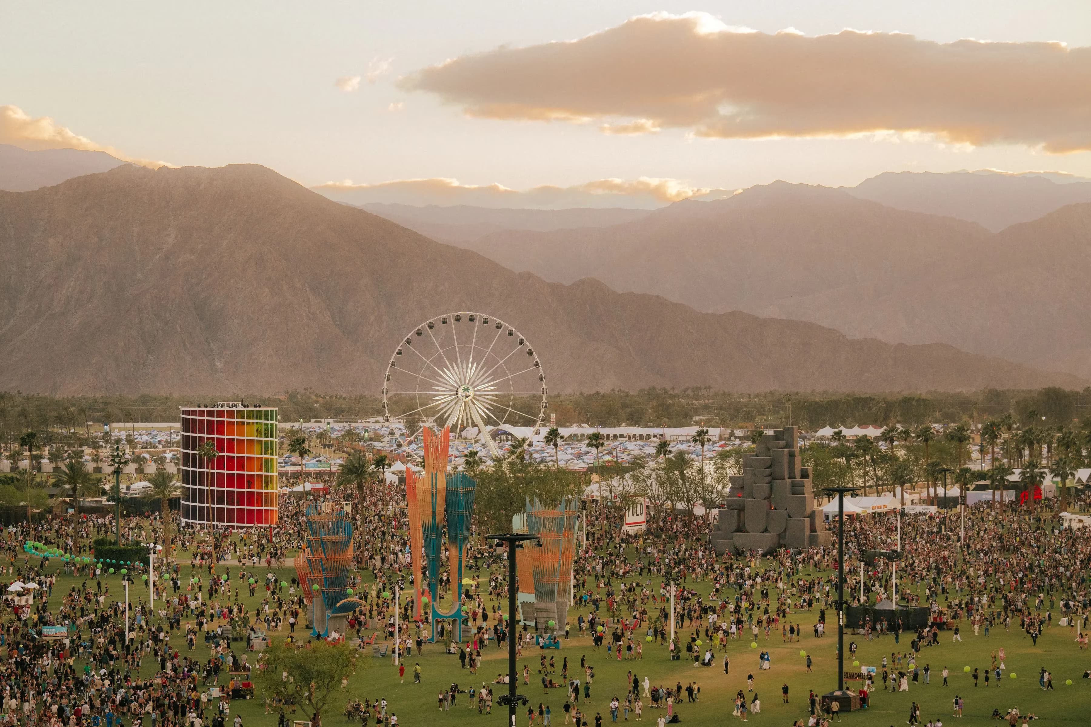 Aerial view of Empire Polo Club at golden hour during Coachella 2026, showing the Ferris wheel, art installations, and crowds in front of the desert mountains.