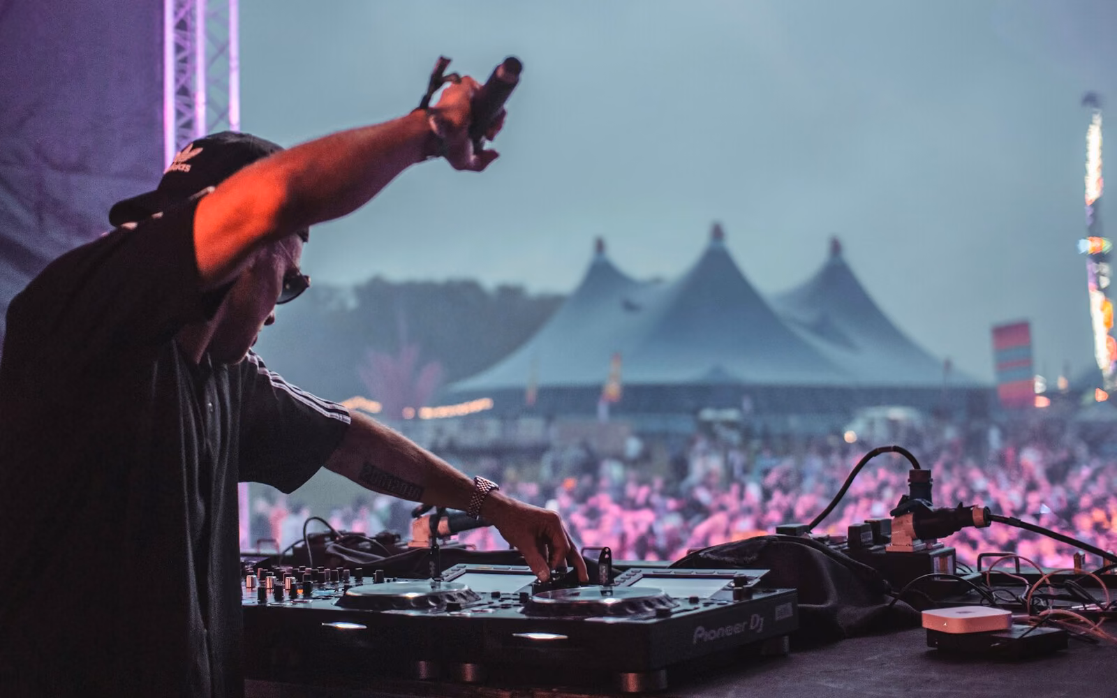 A DJ raises a microphone above the decks as the Sahara tent and crowd glow pink behind him, Coachella 2026.