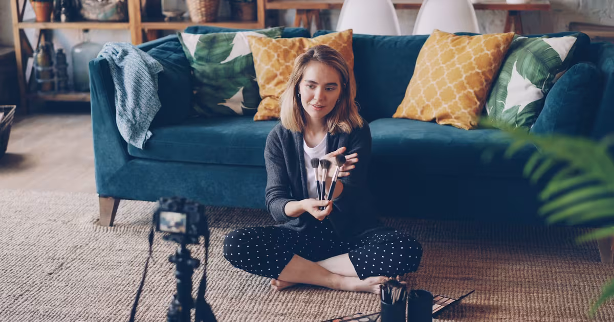 Brand ambassador unboxing branded products and creating content at home, holding merch to camera in a warm, light setting.