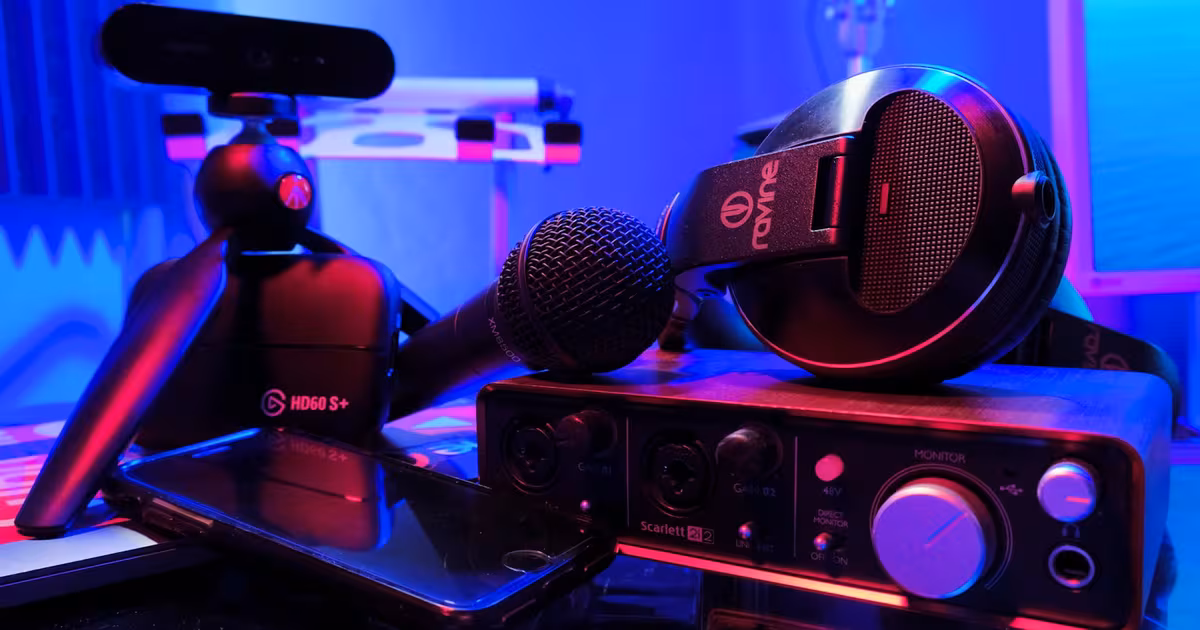 Gaming content creator live streaming with an RGB-lit setup and dual monitors, headset on, capture-card gear on the desk and chat visible on screen.