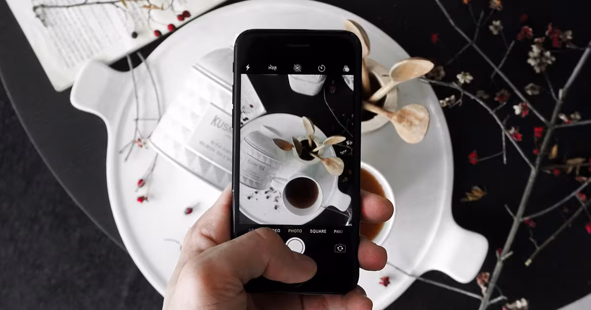 Food influencer photographing a styled brunch plate with a smartphone for Instagram, overhead flat-lay in warm natural light.