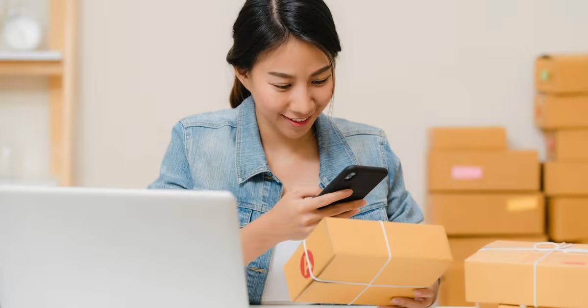 Startup founder packing product seeding boxes for nano-influencers on a small budget, with branded product, shipping boxes, handwritten notes and discount-code cards on a desk.